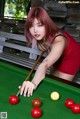 A woman in a red dress is playing pool.