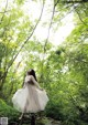 A woman in a white dress standing on a rock in the woods.