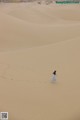 A woman in a blue dress walking across a sand dune.