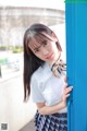 A young woman in a school uniform leaning against a blue door.