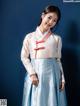 A woman in a blue and white hanbok poses for a picture.