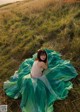 A woman in a green dress sitting in a grassy field.