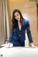 A woman in a blue suit leaning on a table.