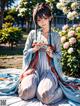 A woman in a blue kimono sitting on a blanket in a park.