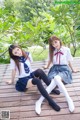 Two young women in school uniforms sitting on a wooden deck.