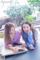 Two young women sitting at a table reading a book.