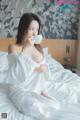 A woman in a white robe sitting on a bed drinking from a cup.