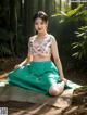 A woman in a green skirt sitting on a blanket in the woods.