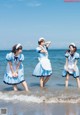 A group of three girls in blue and white dresses on the beach.