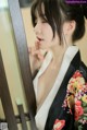 A woman in a black and white kimono leaning against a mirror.