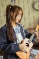 A woman in a school uniform playing a ukulele.