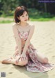 A woman sitting on the sand in a floral dress.