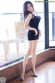 A woman in a black dress posing by a window.