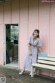 A woman standing next to a bench in front of a pink building.