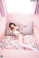 A woman laying on a bed covered in pink and white balloons.