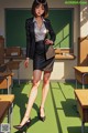 A woman in a black skirt and blazer standing in a classroom.